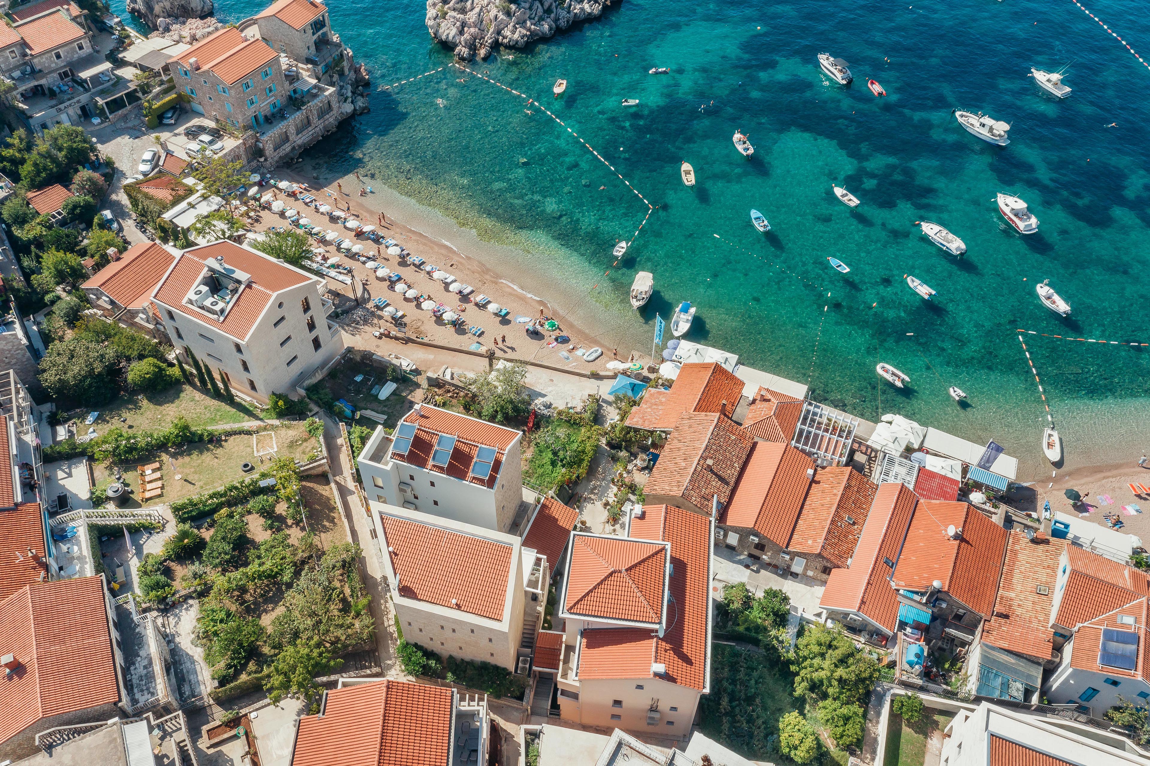 Breathtaking aerial view of a coastal village in Montenegro with vibrant red-tiled roofs and turquoise waters.